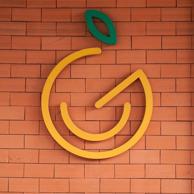 Detalhe do ícone amarelo do Gepetto, com a folhinha verde, aplicado na parede de tijolinho da loja.